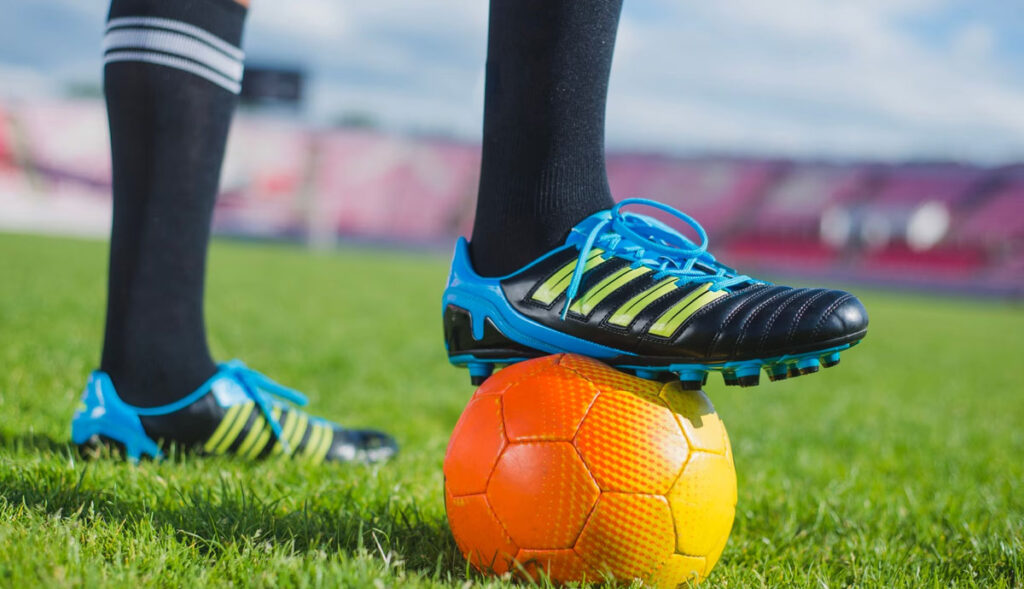 fotbalové kopačky na noze, která stojí na fotbalovém míči - ilustrační obrázek pro to, jak vybrat kopačky